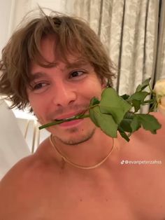 a shirtless man holding a rose up to his face and looking at the camera