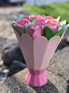 a pink vase filled with paper flowers sitting on top of a rock