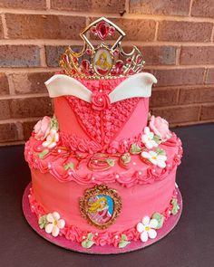 a pink cake with a tiara on top sitting in front of a brick wall