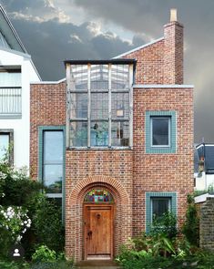 a brick building with an arched wooden door and window panes on the front, surrounded by greenery