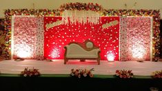 a stage set up for a wedding ceremony with red and white flowers on the wall