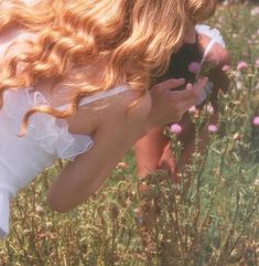 a woman in a white dress is taking a picture with her cell phone while standing in a field full of wildflowers