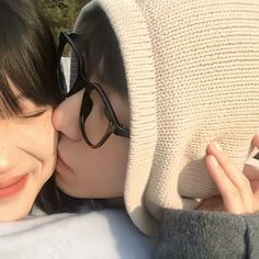 two women are kissing each other while wearing glasses and sweaters, both with their faces close to the camera