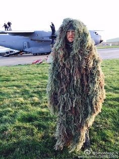 a man dressed in camouflage standing next to an airplane