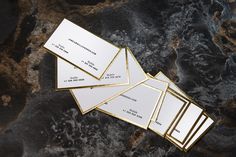 five business cards laying on top of a marble surface with gold trimmings and white paper