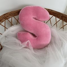 a pink pillow sitting on top of a bed next to a wicker basket filled with white tulle