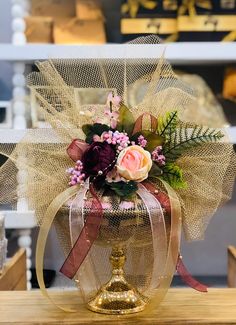 a gold vase with flowers in it sitting on a wooden table next to other items