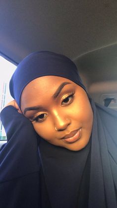 a woman wearing a headscarf in the back seat of a car with her hand on her head