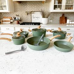 green pots and pans sitting on a kitchen counter top with wooden utensils