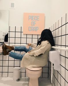 a woman sitting on top of a toilet next to a wall with black and white tiles