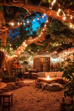 an outdoor living area with lights strung over the trees and couches on the ground