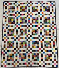 a multicolored patchwork quilt on a white sheet with black border and two rows of squares