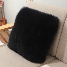 a black fur pillow sitting on top of a couch next to a wooden table and guitar