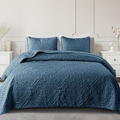 a bed with blue bedspread and pillows in a white walled room next to two nightstands