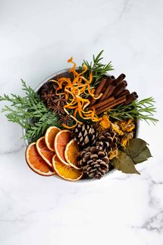 an arrangement of oranges, cinnamon sticks and pine cones on a white marble surface