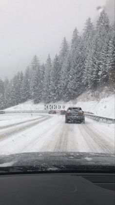 a car driving down a snow covered road in the middle of winter with trees on both sides