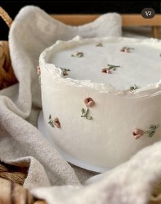 a white cake with pink flowers on it sitting on a plate next to a basket