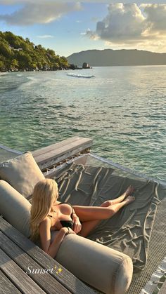 a woman laying on top of a wooden deck next to the ocean