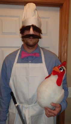 a man in an apron holding a chicken with a fake mustache on it's head