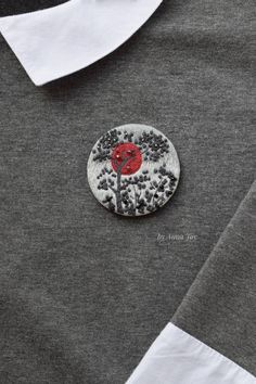 a button with a red flower on it sitting on top of a gray shirt and white collar