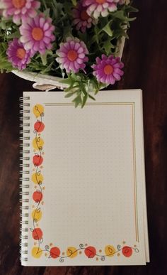 an open notebook sitting on top of a wooden table next to purple and yellow flowers