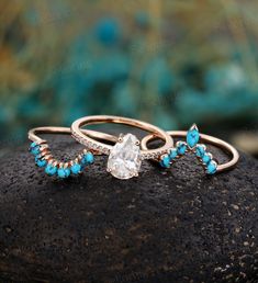 two gold rings with turquoise stones and diamonds on top of a rock in front of a blue background