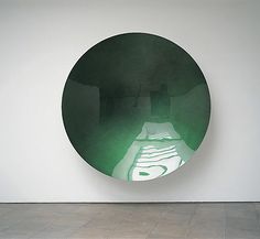 a round mirror hanging on the wall next to a white wall with a painting in it