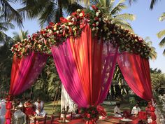 an outdoor ceremony with red and pink draping, white flowers and greenery