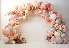 an arch made out of balloons and flowers on the floor in front of a white wall