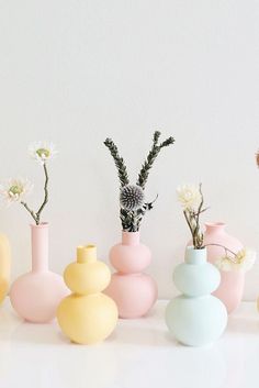 several different colored vases with flowers in them on a table top next to a white wall