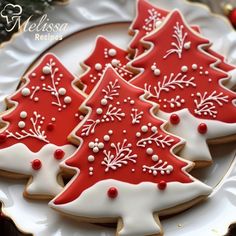 three decorated christmas tree cookies on a white plate with red and white frosted decorations