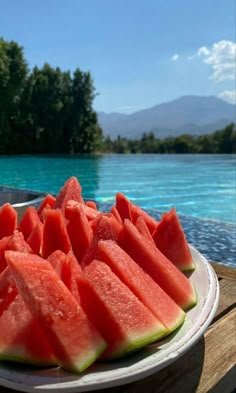 slices of watermelon are on a white plate near the edge of a pool