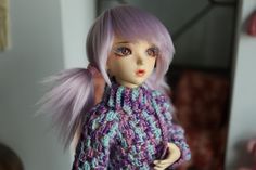 a doll with purple hair wearing a knitted sweater and holding her hand on her hip