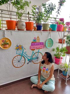 a woman sitting on the floor in front of a wall with potted plants