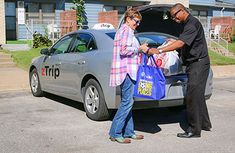 a man and woman loading groceries into the trunk of a car in front of a house