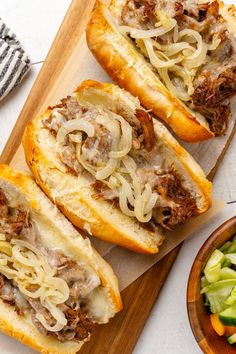 three sandwiches with meat, cheese and onions on a cutting board next to a bowl of salad