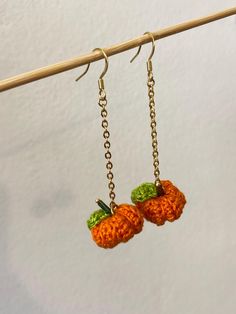 two crocheted oranges hanging from hooks on a clothes line with wooden pegs