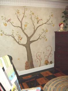 a room with a tree painted on the wall and stuffed animals sitting in chairs next to it