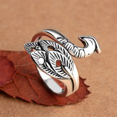 a silver ring sitting on top of a leaf covered ground next to a red leaf