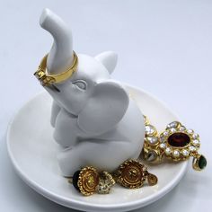 an elephant figurine sitting on top of a white plate with gold jewelry around it