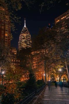 people walking down the sidewalk in front of tall buildings at night with lights shining on them