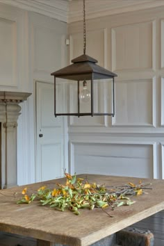 a light hanging over a wooden table in a room with white walls and wood flooring