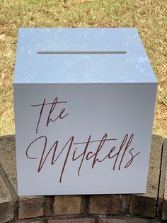 a white box sitting on top of a brick wall next to a grass covered field