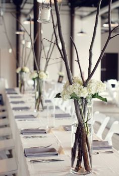 the table is set up with white flowers and branches in vases on each side