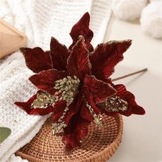 a red poinsettia in a woven basket on a white tablecloth next to knitting needles