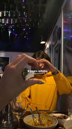 a woman in a yellow jacket is eating food at a table with two hands on her face