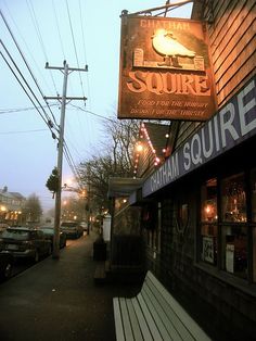 a restaurant sign hanging from the side of a building next to a sidewalk with parked cars