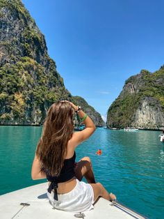 a woman sitting on the bow of a boat looking out at mountains and blue water