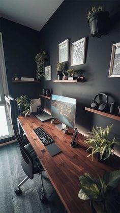 a desk with a computer on it in front of a window and some potted plants