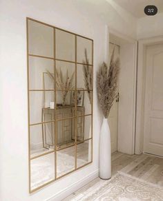 a tall white vase sitting next to a mirror on top of a wooden floor in front of a door